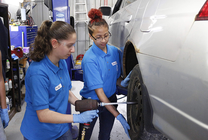 Two young women changing a car tire in The Shop